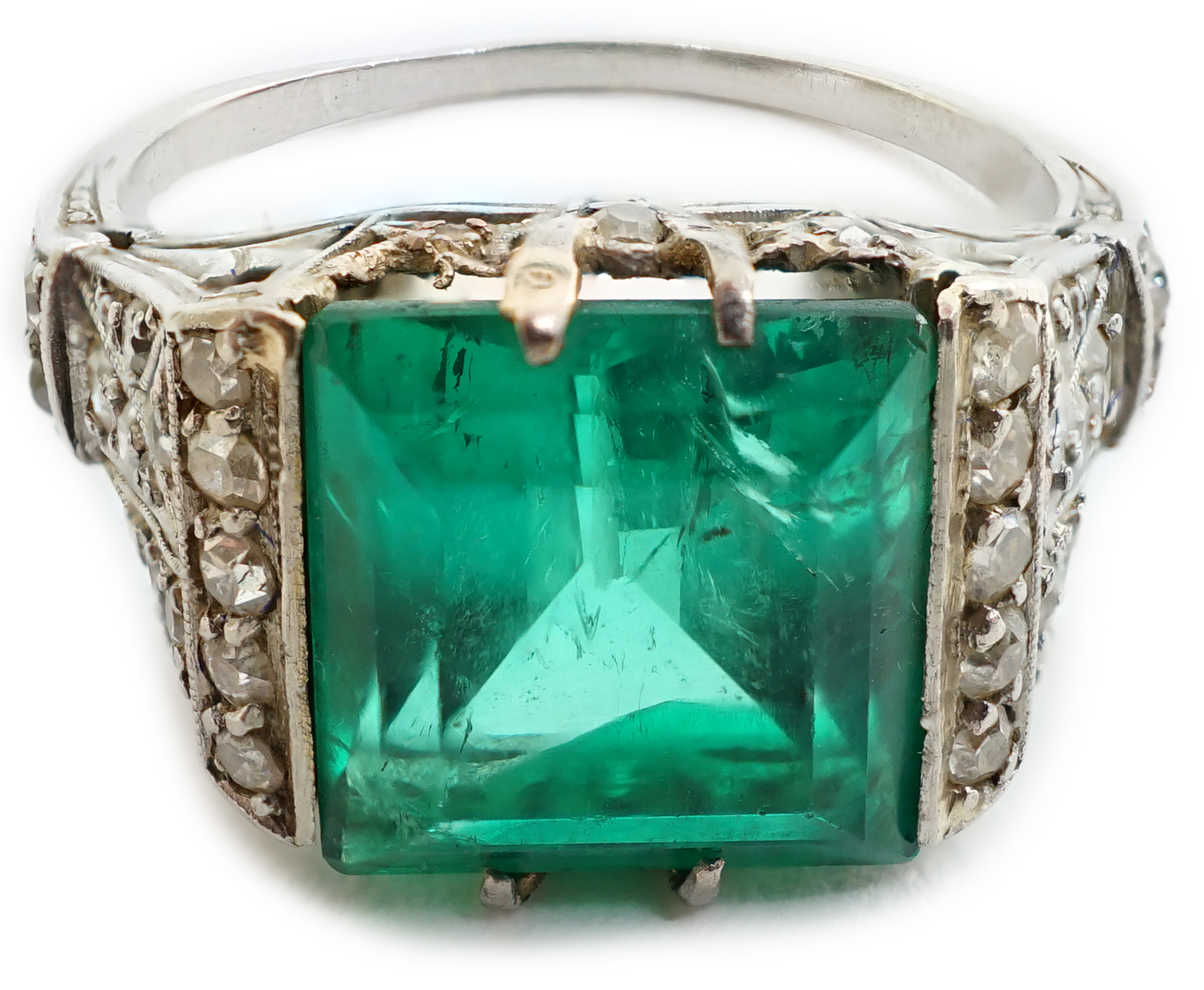 A 1920's/1930's platinum and square cut emerald set dress ring, with pierced and millegrain diamond cluster set shoulders